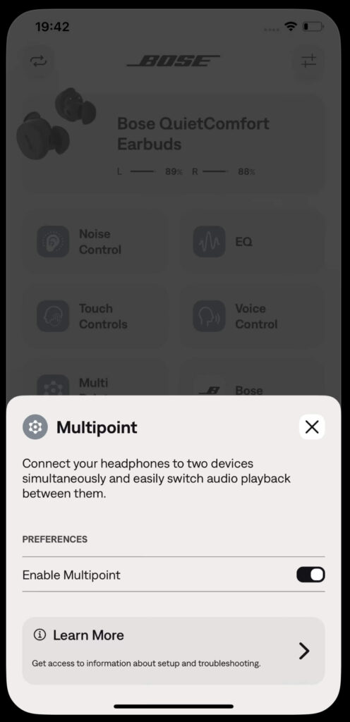 Multipoint settings screen in the Bose QuietComfort Earbuds app. The screen describes the multipoint feature for connecting headphones to two devices simultaneously. A toggle switch to enable multipoint is visible, set to ‘on.’ A ‘Learn More’ link appears at the bottom for troubleshooting and setup guidance.