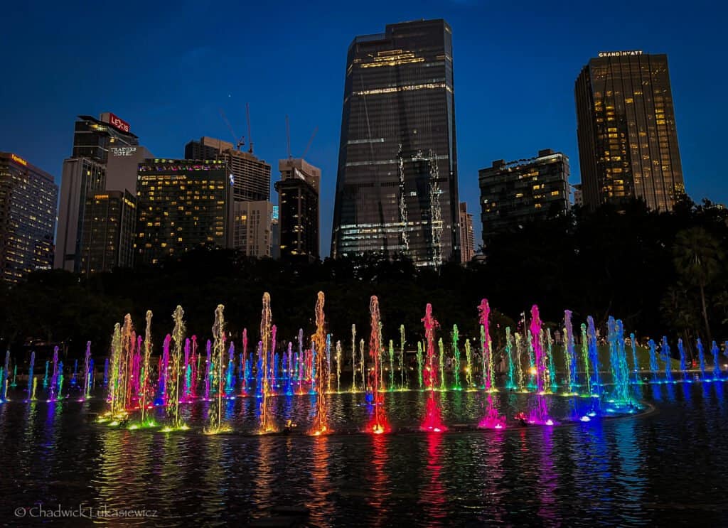 Colorful illuminated fountains of Lake Symphony at KLCC Park in Kuala Lumpur, Malaysia, with modern skyscrapers glowing against the evening sky.