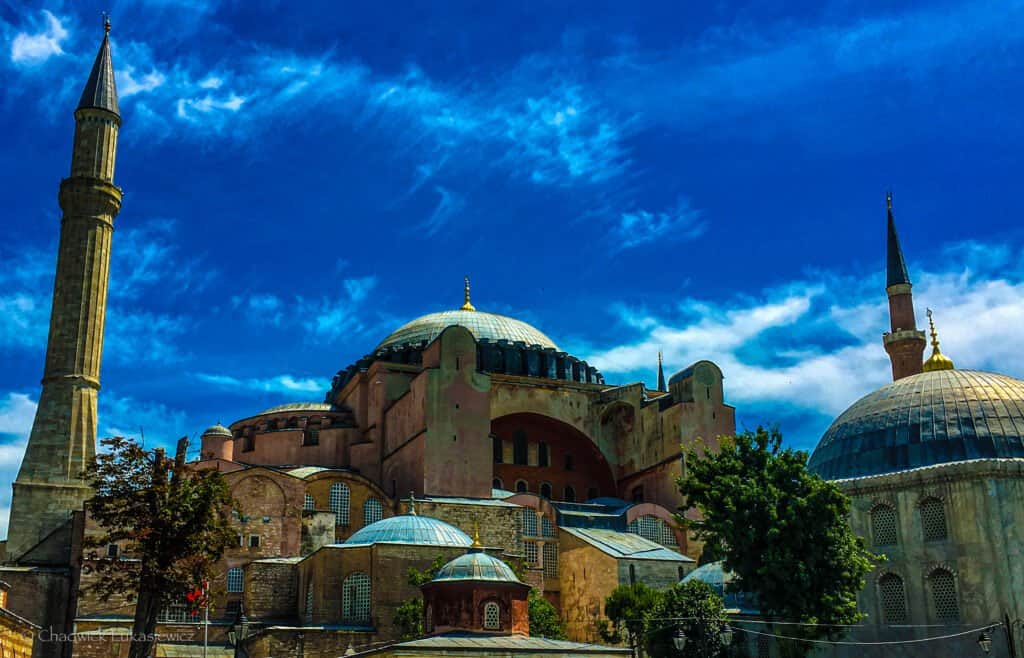 Hagia Sophia in Istanbul, Turkey, with its large domes and minarets set against a bright blue sky with wispy clouds