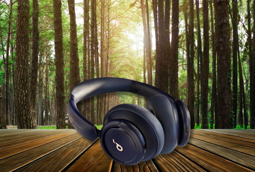 A pair of black Soundcore Life Q30 headphones by Anker placed on a wooden table, set against a serene forest backdrop with sunlight streaming through tall trees.