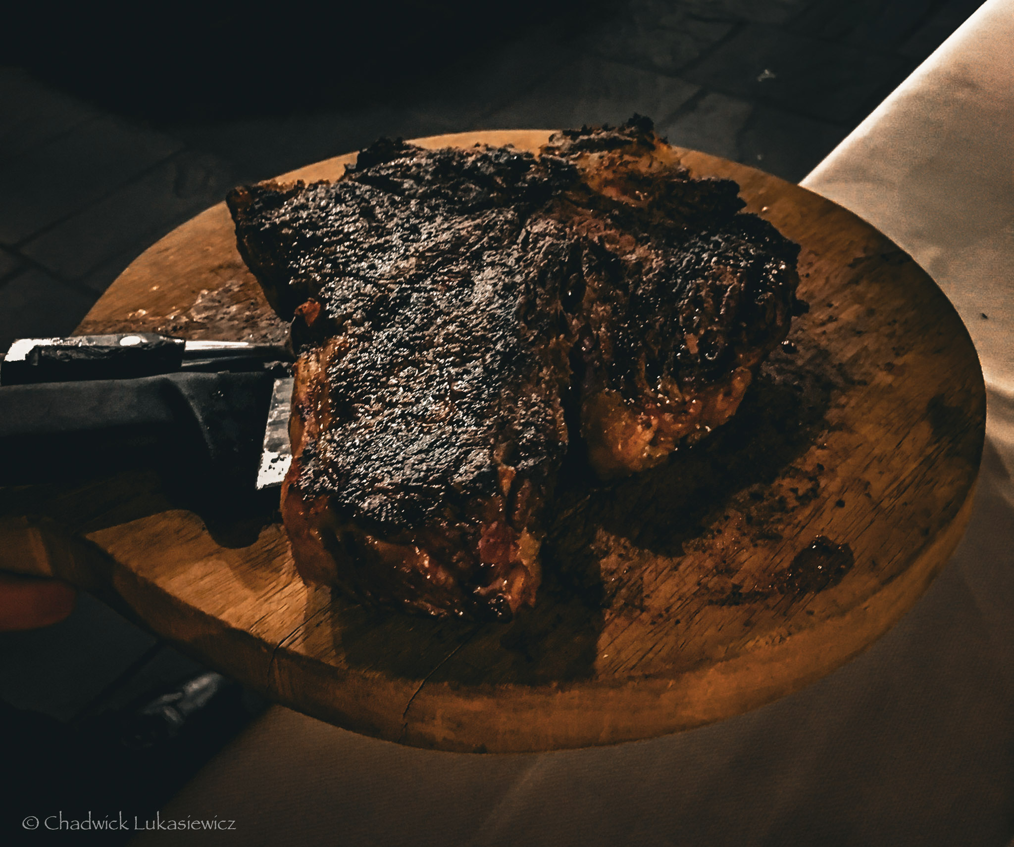 A perfectly seared steak served on a rustic wooden board, showcasing a charred crust and juicy interior, lit by a warm, ambient glow.