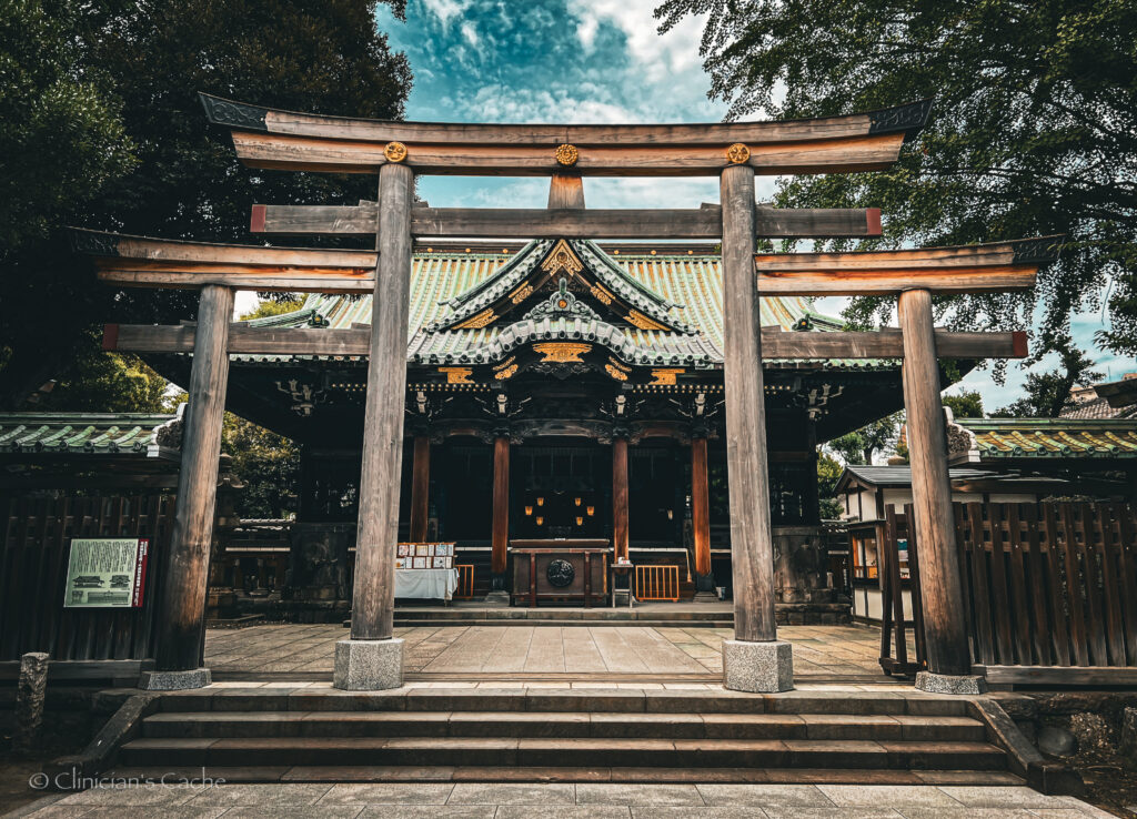 Traditional Japanese shrine with ornate architecture, viewed through a large wooden torii gate, surrounded by trees in Tokyo, Japan.