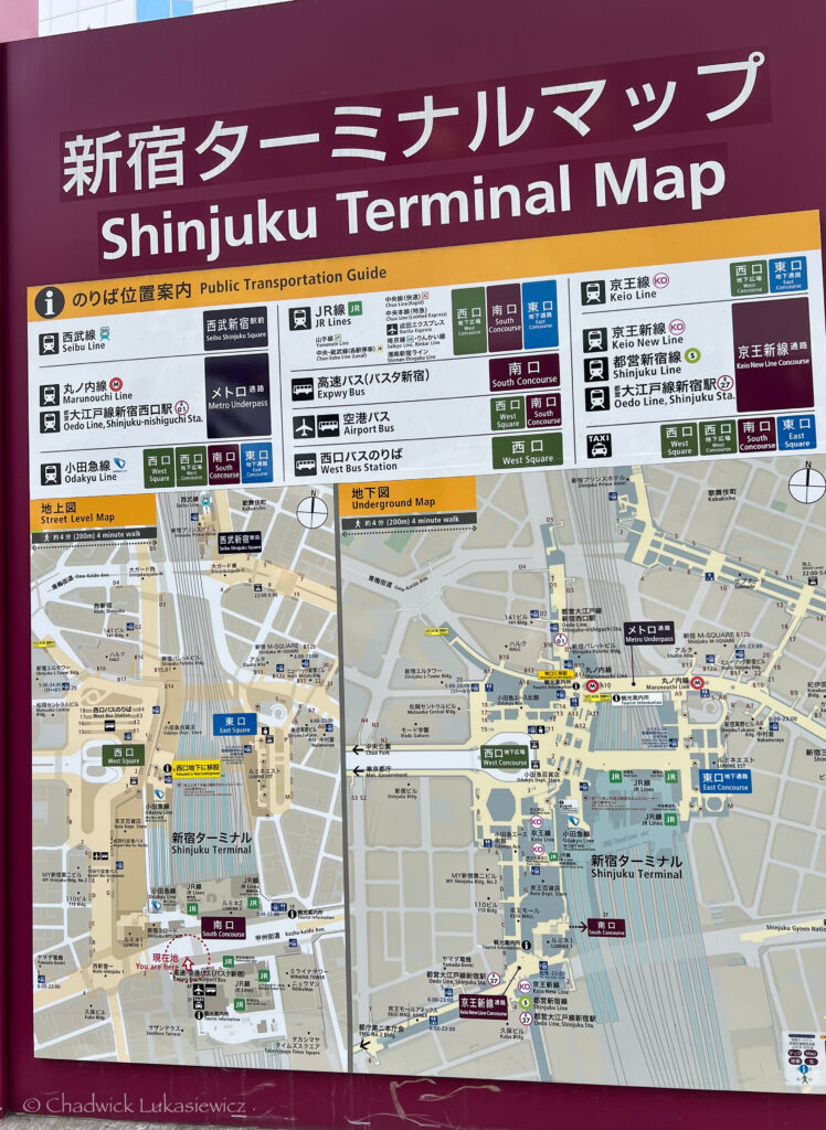 A detailed map and guide for navigating Shinjuku Terminal in Tokyo, Japan, displayed on a large sign with Japanese and English text. The top section provides a public transportation guide, showing color-coded icons and names for various train lines like the JR Lines, Keio Line, and Oedo Line. Key areas such as the South Concourse, West Square, and East Square are labeled. Below, two maps illustrate the terminal’s layout, with a “Street Level Map” and “Underground Map” featuring pathways, exits, and nearby facilities. The sign’s color scheme includes maroon, yellow, and green, with “Shinjuku Terminal Map” in bold white letters at the top.