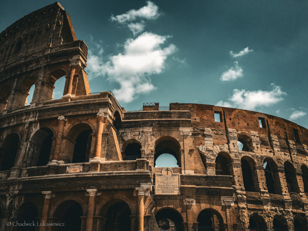 An iconic view of the Colosseum in Rome, Italy, captured under a bright sky with scattered clouds. The sunlight illuminates the ancient arches and weathered stone facade, showcasing the grandeur and history of this monumental amphitheater. Perfect imagery for an ADHD travel guide to Rome and Athens, highlighting captivating landmarks that inspire awe.