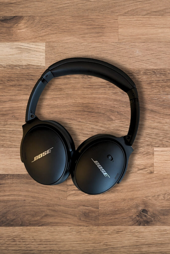 Black Bose QuietComfort 45 headphones lying flat on a wooden surface, with the ear cups fully visible. The matte finish of the headphones reflects subtle light.