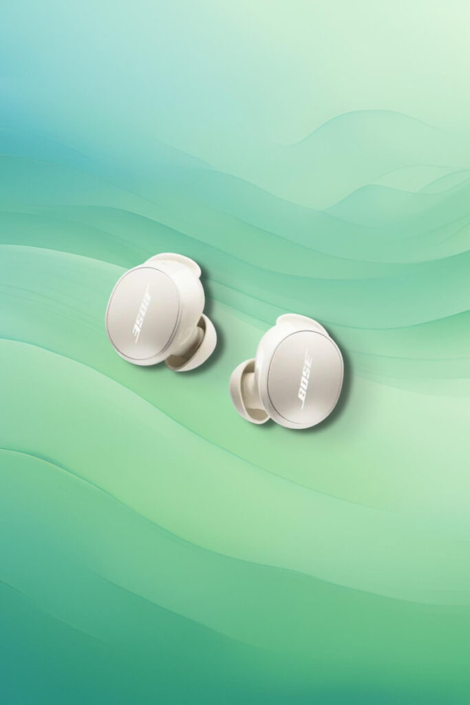 A pair of Bose QuietComfort Earbuds in white, displayed against a soft green gradient background. The sleek, oval-shaped earbuds feature the Bose logo on each surface, emphasizing their premium design and compact form factor.