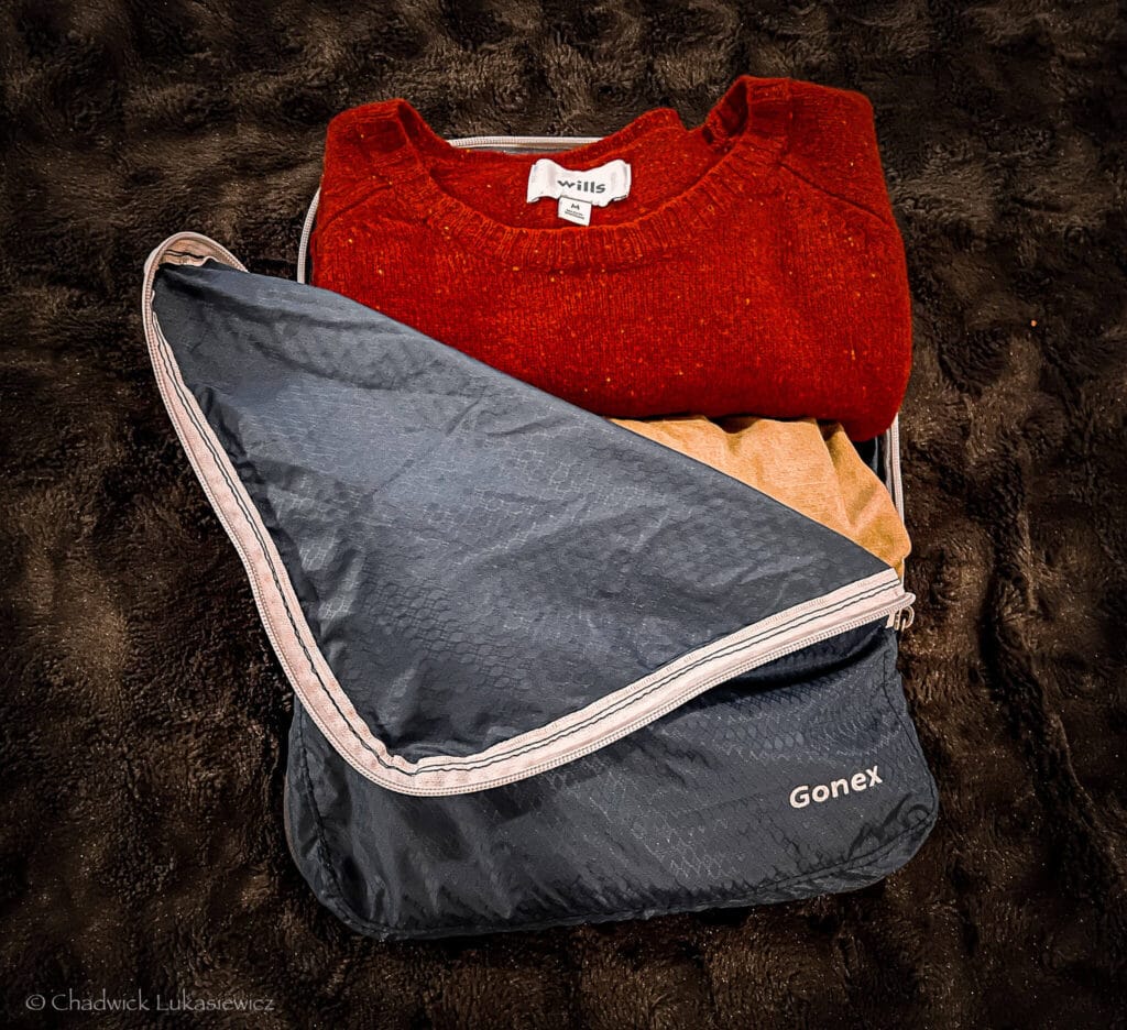Navy blue Gonex compression cube packed with a red sweater, beige pants, and other clothing, showcasing minimalist packing for ADHD travelers