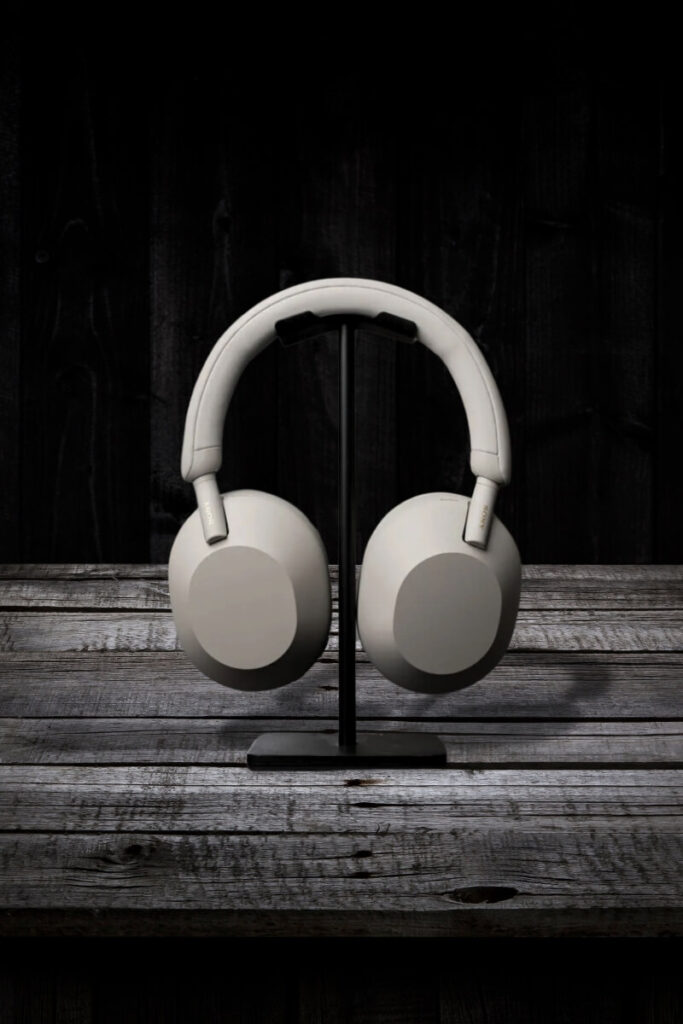 White Sony WH-1000XM5 headphones displayed on a black stand, positioned on a rustic wooden table with a dark, moody backdrop