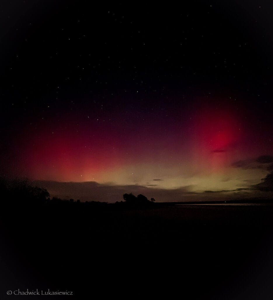 Red and green aurora borealis illuminating the night sky over Jackson Lake State Park, Colorado, with stars twinkling above.