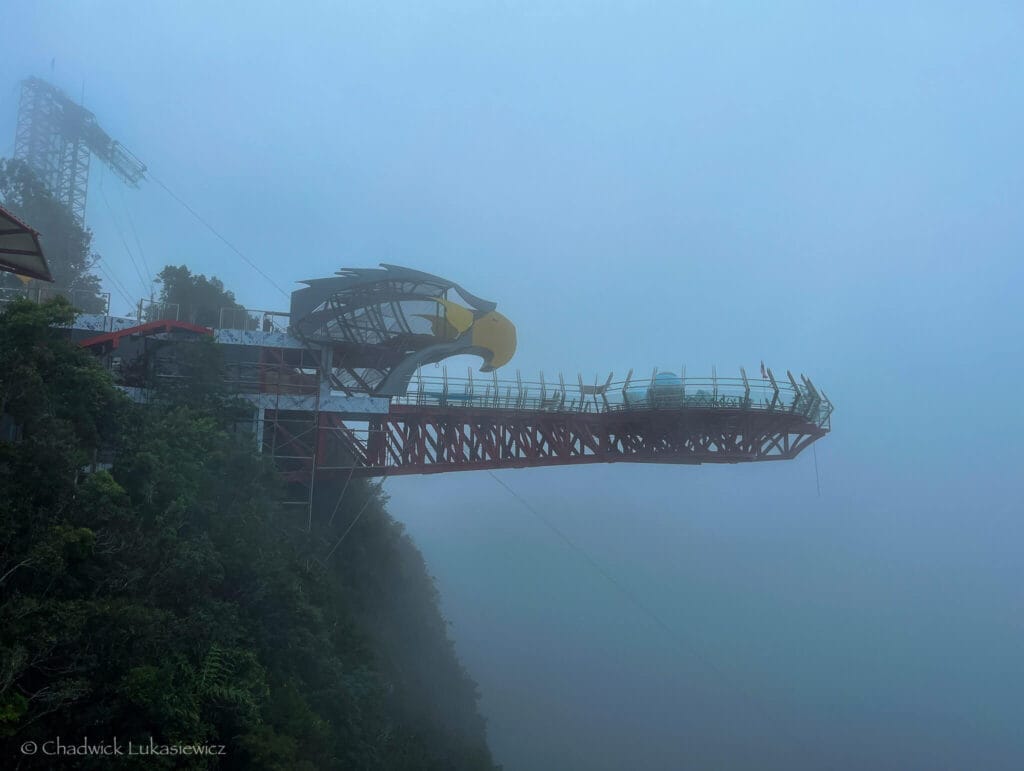 The Langkawi Sky Bridge in Malaysia disappears into dense fog, demonstrating smartphone camera features like Night Mode and RAW capture for low-light photography.