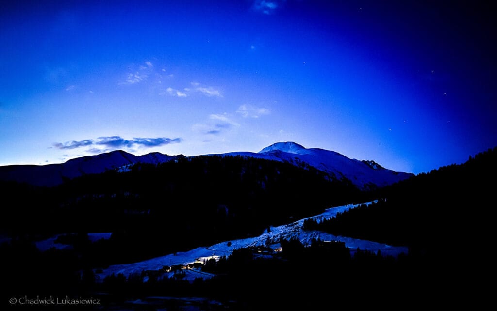 Before sunrise in Sedrun, Switzerland, the alpine slopes glow under a deep blue sky, capturing the hyperfocus of an ADHD travel photographer at dawn.